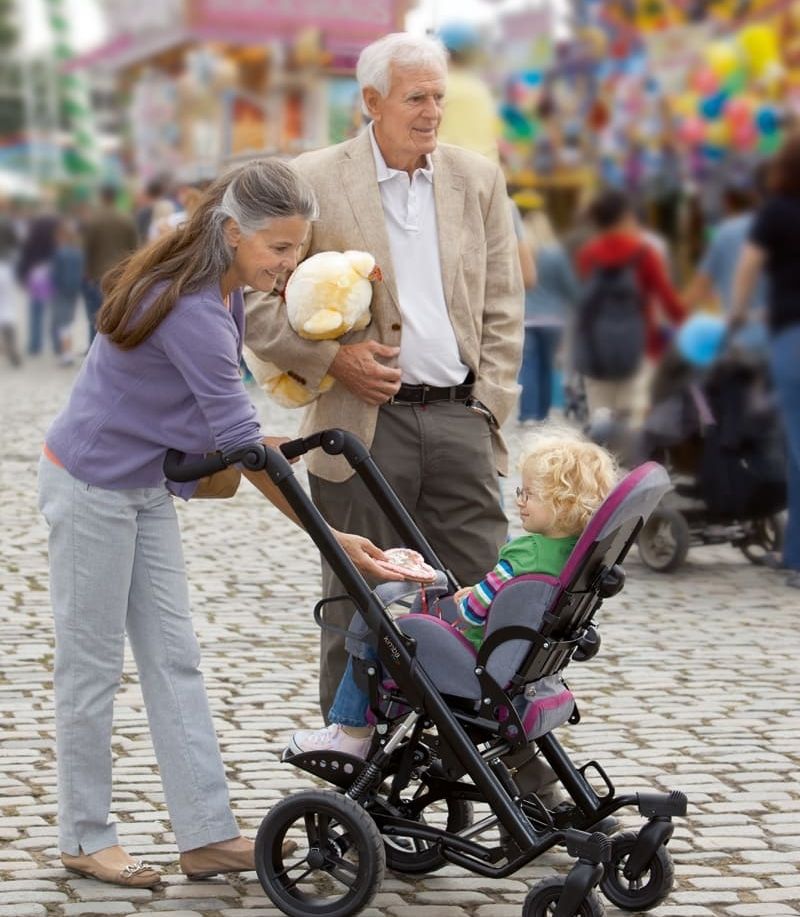 Ein Kind im Rollstuhl ist mit den Großeltern auf einer Kirmes