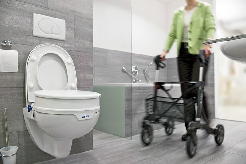 Eine Frau mit einem Rollator geht zur Toilette mit einer Toilettensitzerhöhung